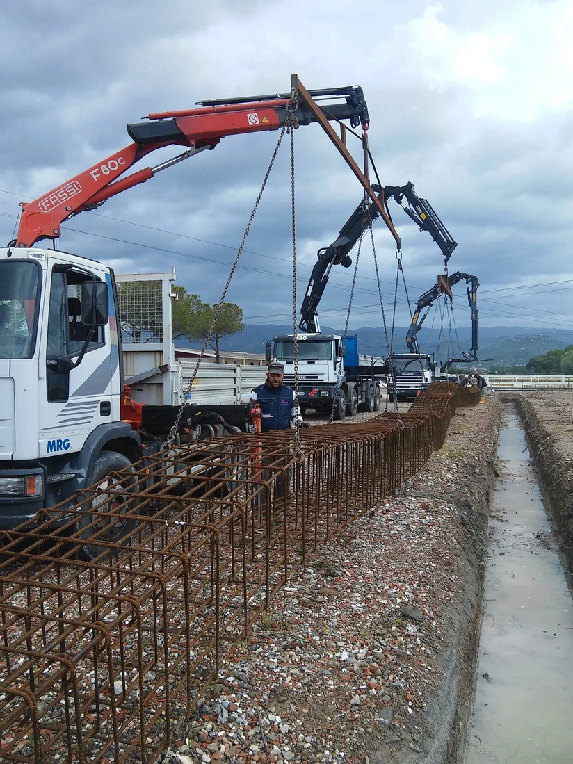 Autocarro con gru MRG durante la posa di gabbie d'armatura in uno scavo di fondazione